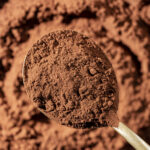 Natural dark brown cocoa powder in spoon in the background, top view, closeup. Heap of organic cacao powder