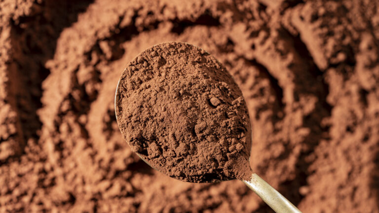 Natural dark brown cocoa powder in spoon in the background, top view, closeup. Heap of organic cacao powder